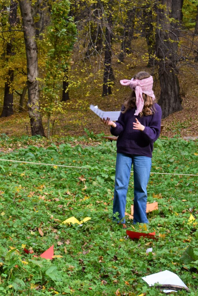 dziewczyna z zasłoniętymi oczami idzie przez park, w ręku trzyma kartkę