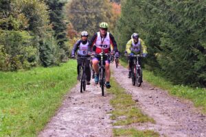 rowerzyści jadą drogą gruntową pod lekkie wzniesienie