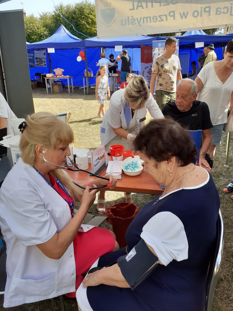 Pielęgniarka mierzy ciśnienie kobiecie, z tyłu pomiar glukozy u mężczyzny