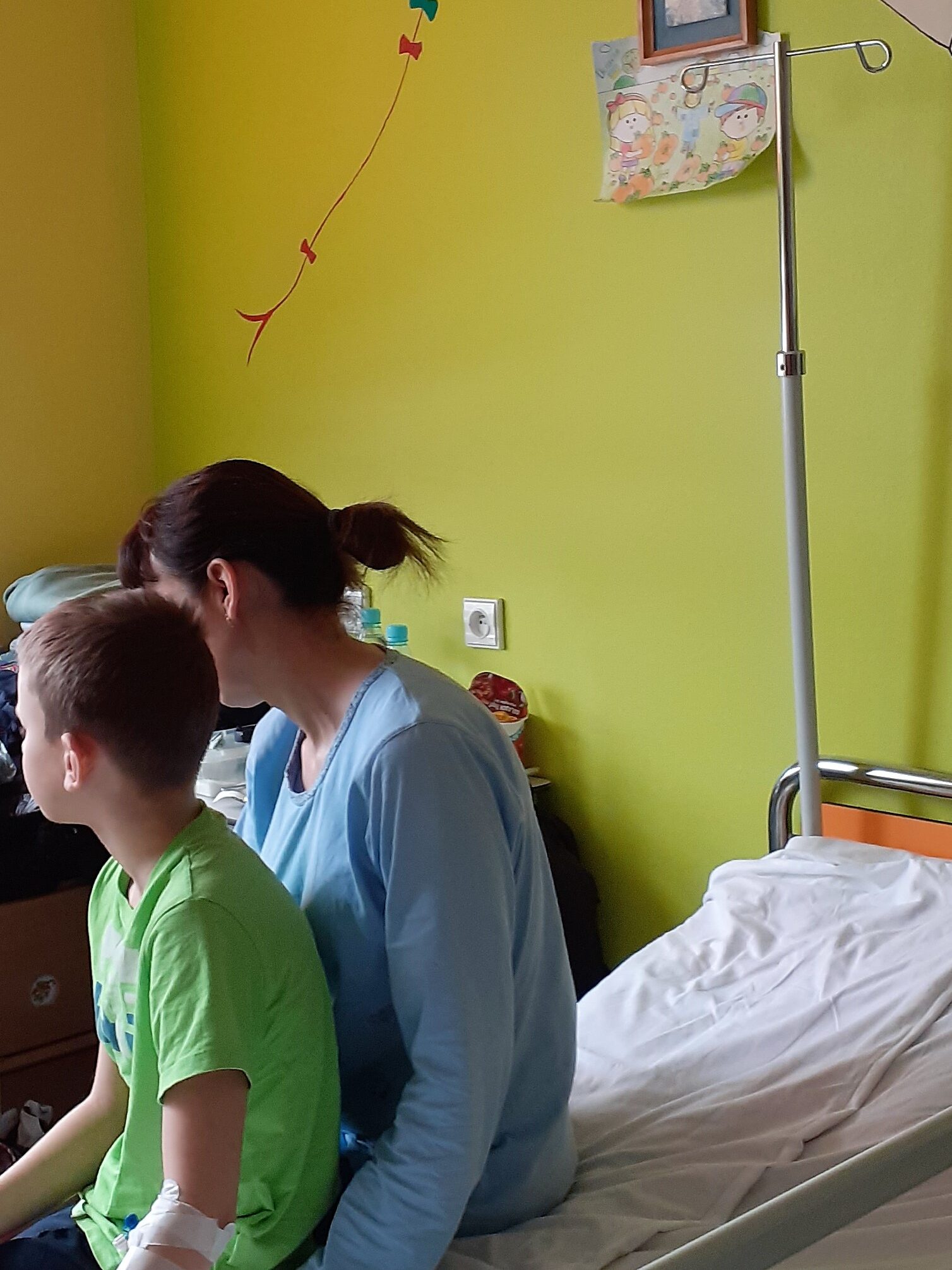 sala szpitalna na pediatrii, na łóżku siedzi kilkuletni chłopiec z mamą, na ścianie postać Lolek z bajki
