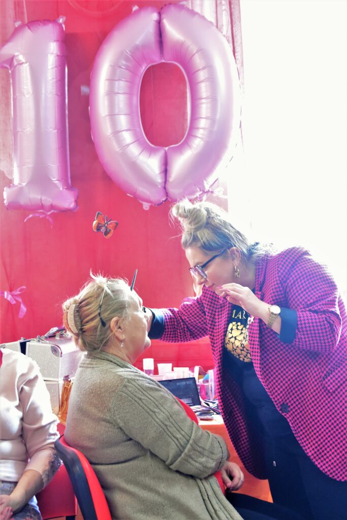 makijażystka maluje kobietę, w tle liczba 10 ułożona z balonów