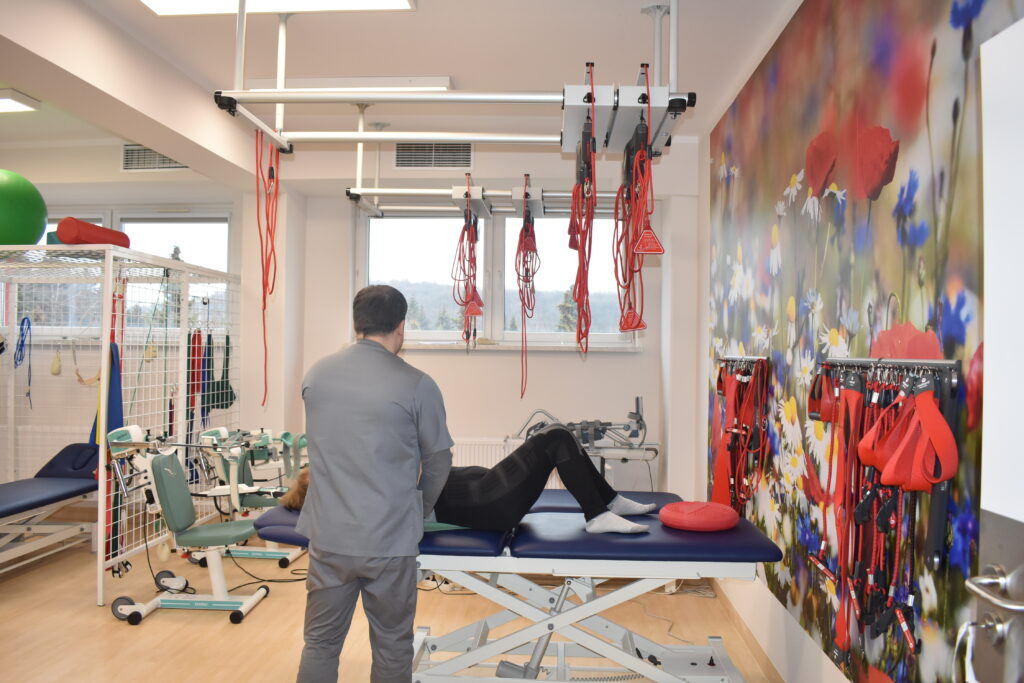 sala ćwiczeń na oddziale rehabilitacji, fizjoterapeuta odwrócony tyłem ćwiczy z pacjentką