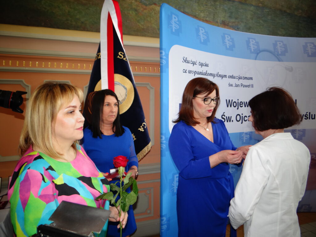 wicewojewoda przypina medal kobiecie, obok stoi dyrektor szpitala z różą
