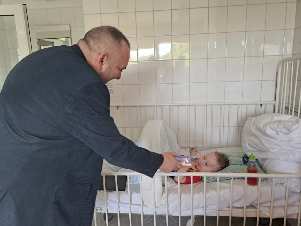 prezes fundacji jerzyk wręcza upominek dziecku leżącemu na szpitalnym łóżku