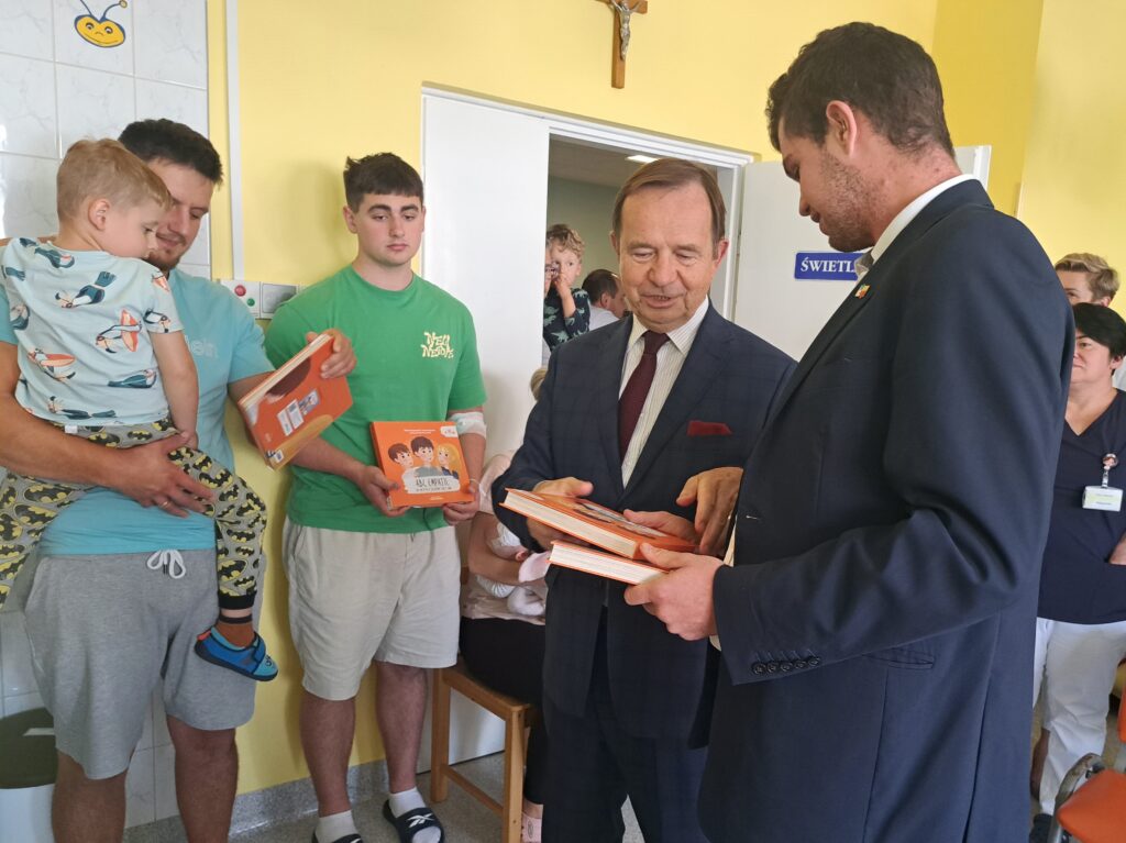 Syn założyciela fundacji podaje książki marszałkowi województwa, na drugim planie mali pacjenci oddziału na świetlicy