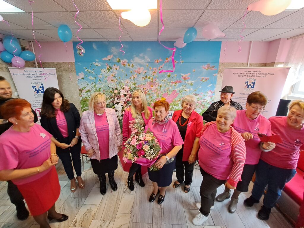 kobiety ubrane w różowe koszulki stoją w półkolu, w centrum kobieta z bukietem kwiatów
