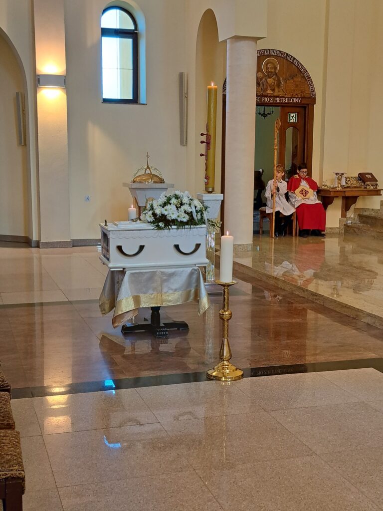 biała nieduża trumna stoi na środku kościoła, obok dwie świece i paschał