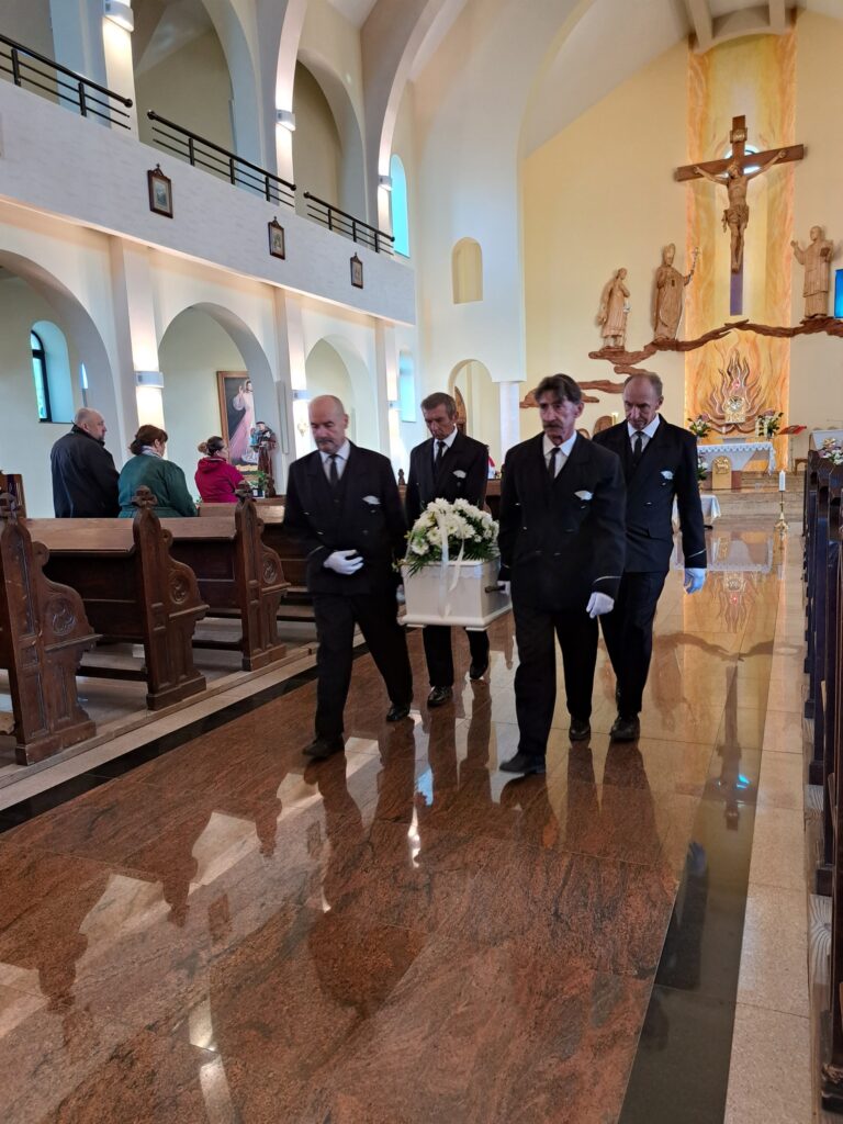 pracownicy zakładu pogrzebowego wynoszą trumnę z kościoła