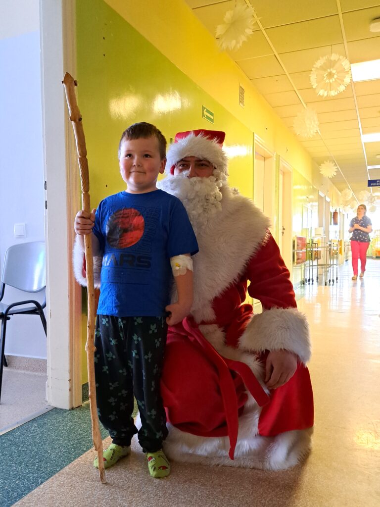 Mikołaj pozuje do zdjęcia z małym chłopcem, chłopiec trzyma w ręce laskę Mikołaja