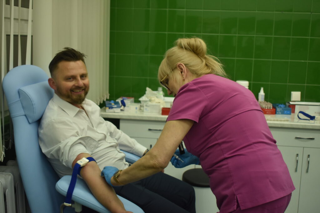 mężczyzna siedzi na fotelu, uśmiecha się, pielęgniarka pobiera krew