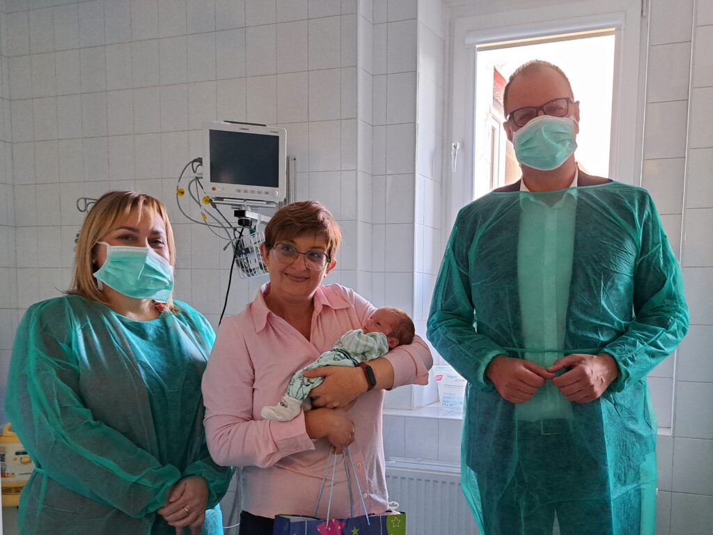 w środku kobieta z noworodkiem na rękach, obok dyrektorka szpitala i prezydent