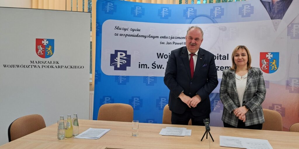 Od prawej: dyrektor Barbara Stawarz i marszałek Piotr Pilch stoją przy stole, za nimi ścianki promocyjne szpitala i urzędu marszałkowskiego