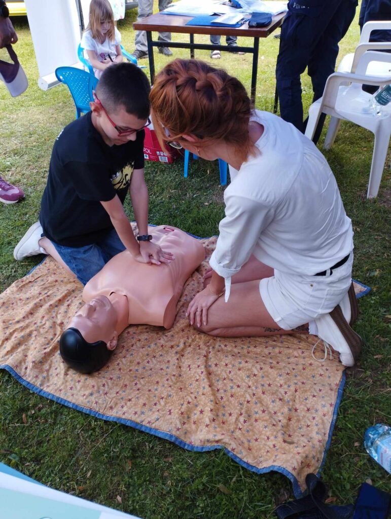 nastoletni chłopiec ćwiczy uciśnięcia na fantomie pierwszej pomocy, obok pielęgniarka