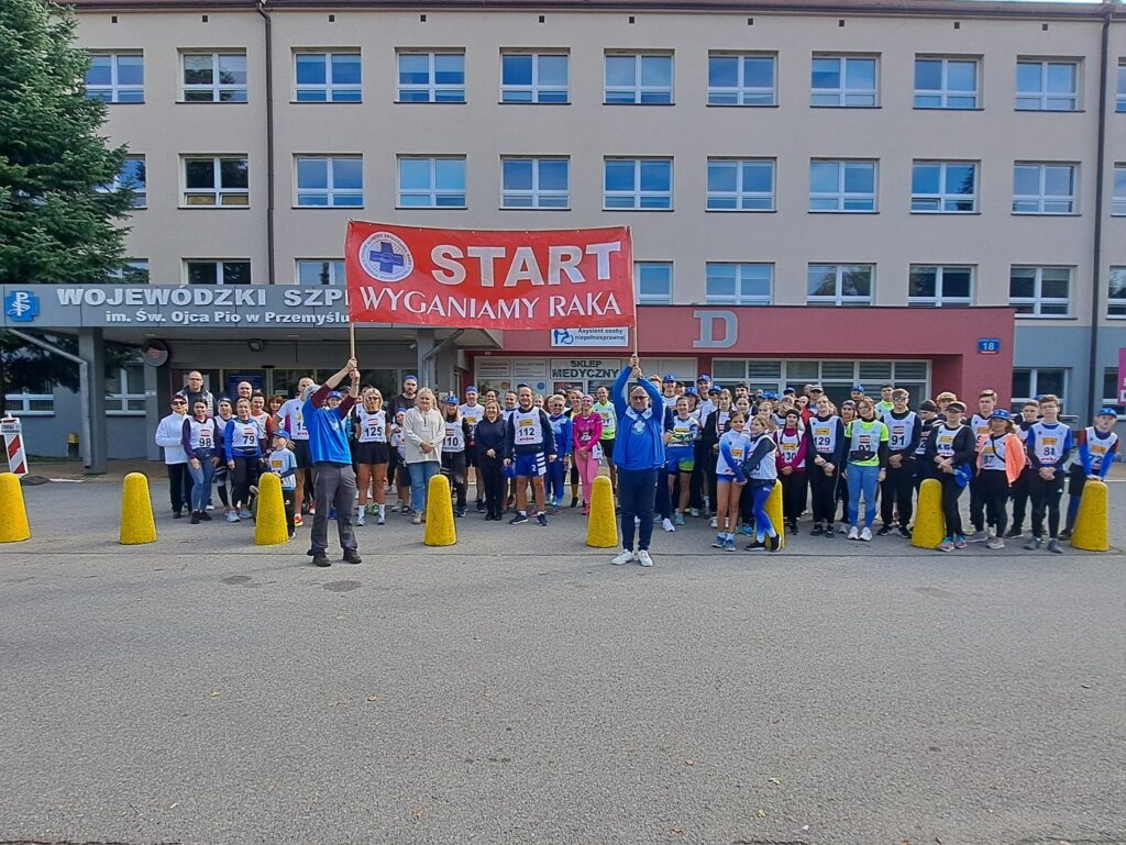 zdjęcie grupowe uczestników biegu przed szpitalem z przodu baner z napisem "START Wyganiamy raka"