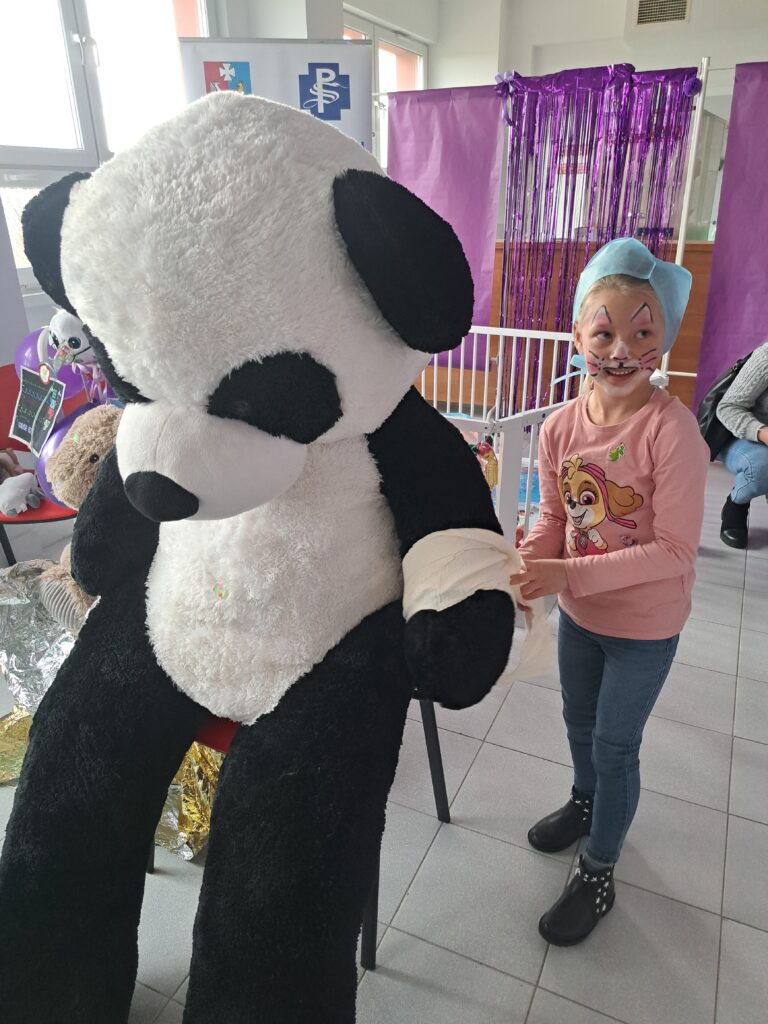 dziewczynka bandażuje dużemu misiowi panda rękę