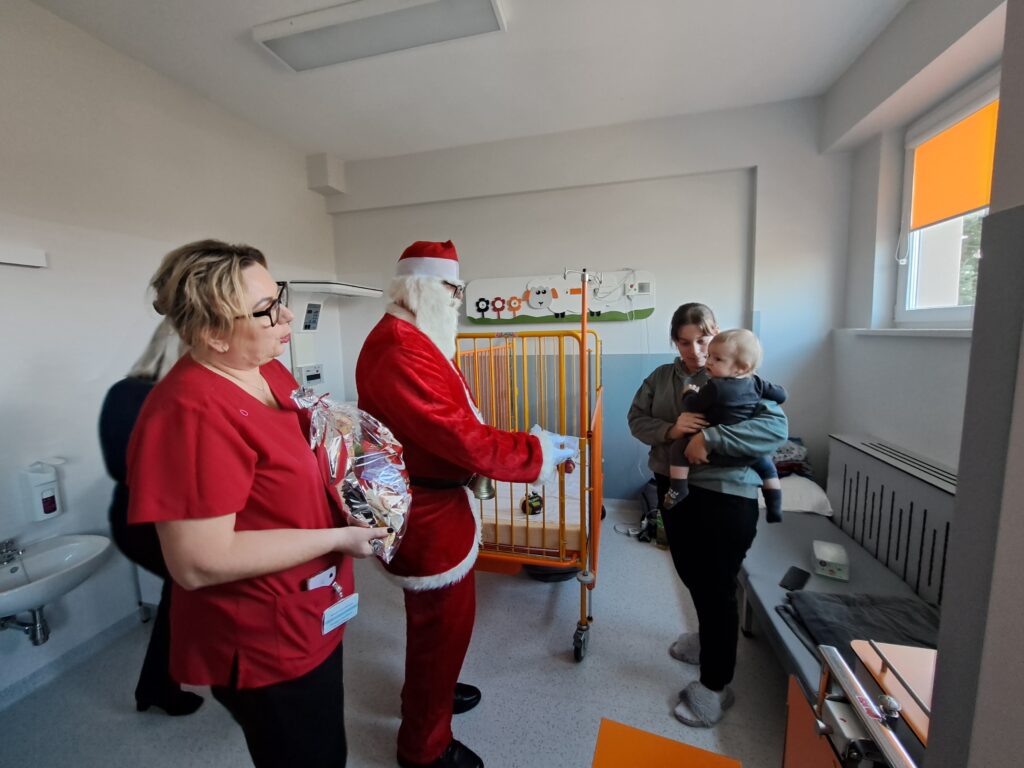 Od lewej zastępca dyrektora z prezentem, Mikołaj i mama z około dwuletnim chłopcem