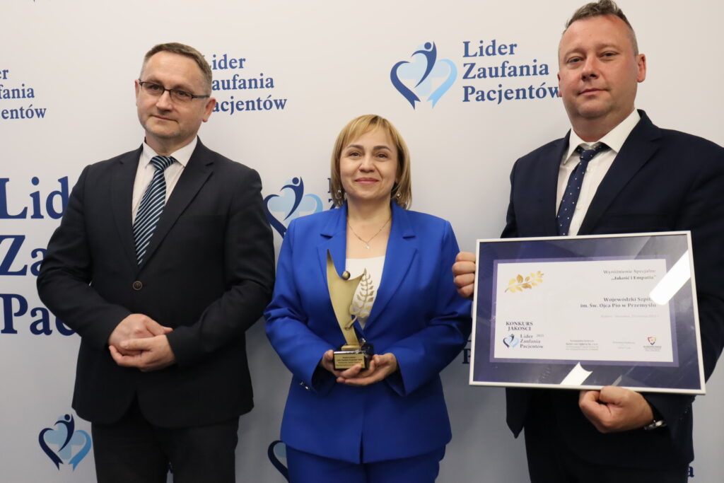 dyrektorka prezentuje statuetkę, obok zastępcy, jeden z nich prezentuje dyplom oprawiony w ramkę