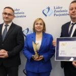 dyrektorka prezentuje statuetkę, obok zastępcy, jeden z nich prezentuje dyplom oprawiony w ramkę
