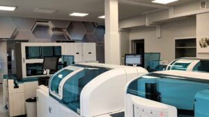 pracownia laboratoryjna, nowoczesne maszyny diagnostyczne w kolorze białym, w tle monitory komputerów, szafki