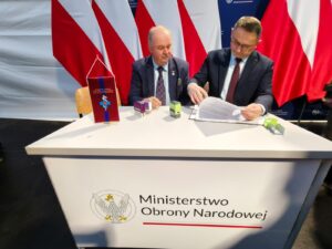 przy stoliku zastepca dyrektora i wicemarszałek województwa podpisują porozumienie, za nimi białoczerwone flagi