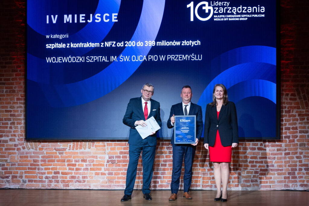 na scenie zastępca dyrektora szpitala odbiera nagrodę, obok kobieta i mężczyzna