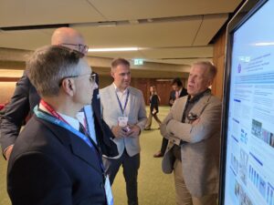 lekarz przy ekranie prezentuje wyświetlany plakat przy grupie kilku słuchaczy