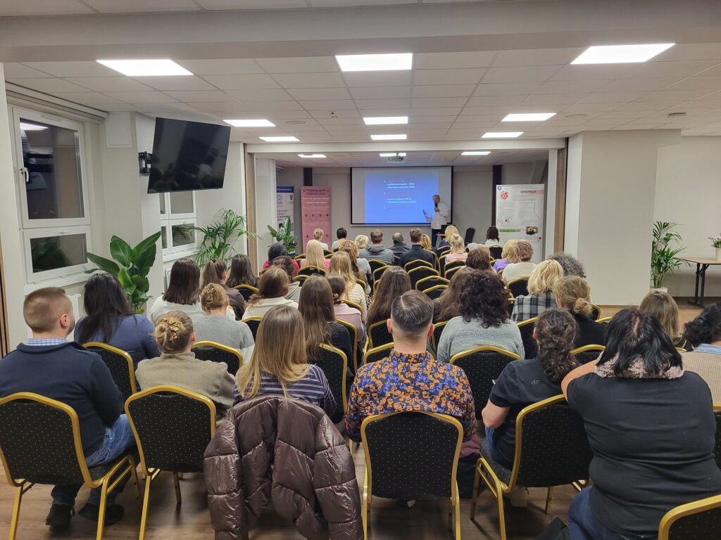 sala wykładowa w tle lekarz-prelegent z prezentacją na ekranie