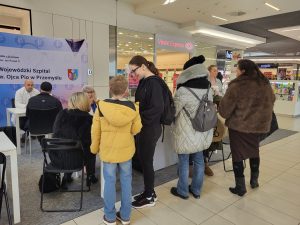 grupa osób stoi przed stoiskiem szpitala w pasażu galerii