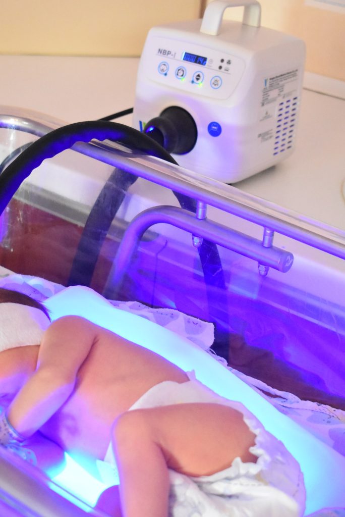 noworodek leży w łóżeczku naświetlany Lampą do fototerapii 