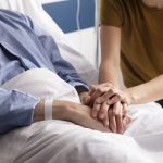 pacjent leżący na łóżku, obok siedzi kobieta, nie widać ich twarzy