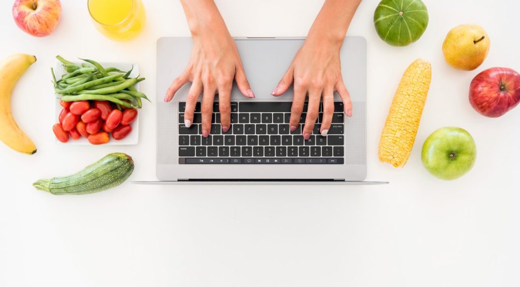 ręce na klawiaturze, wokół owoce i warzywa