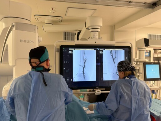 przy stole operacyjnym dwie osoby przeprowadzające zabieg, duży ekran na którym widać obraz żył