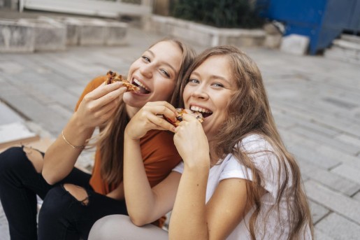 dwie nastoletnie dziewczyny jedzą pizzę na chodniku